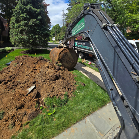 Excavator arm lifting a dirt clump beside a landscaped lawn under a blue sky
