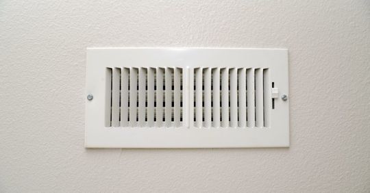 White rectangular air vent on a white wall, with vertical slats.