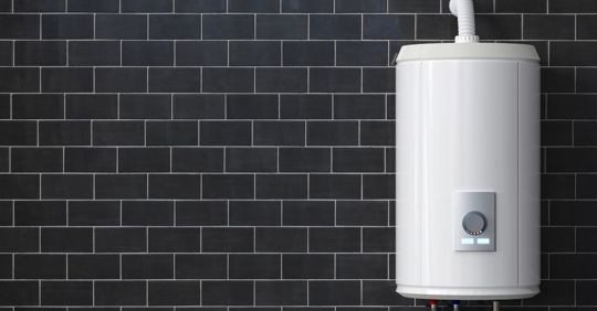 White water heater on a dark tiled wall.