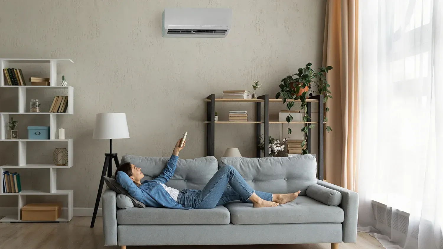 In-wall home air conditioning is pictured above a person reclining on a couch.
