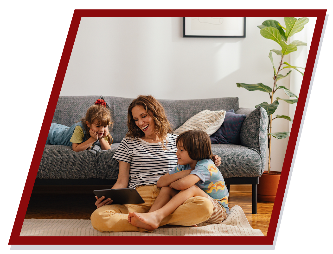Woman and two children sitting on the floor, looking at a tablet in a living room. Woman and two children sitting on the floor, looking at a tablet in a living room.