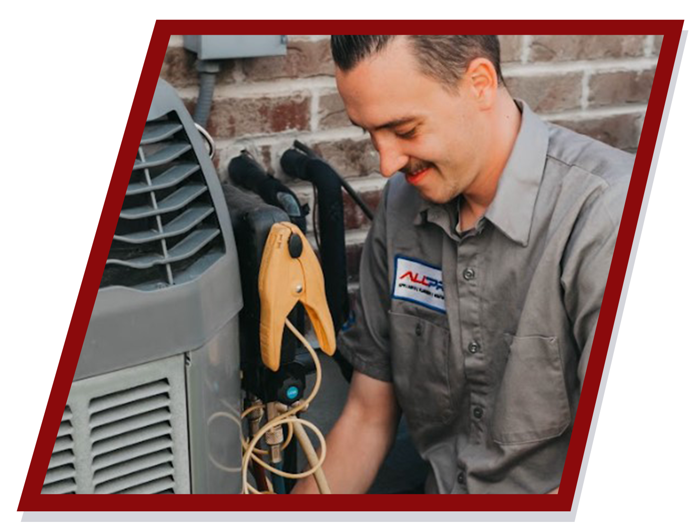 HVAC technician smiling while working on an air conditioning unit outside a brick building.