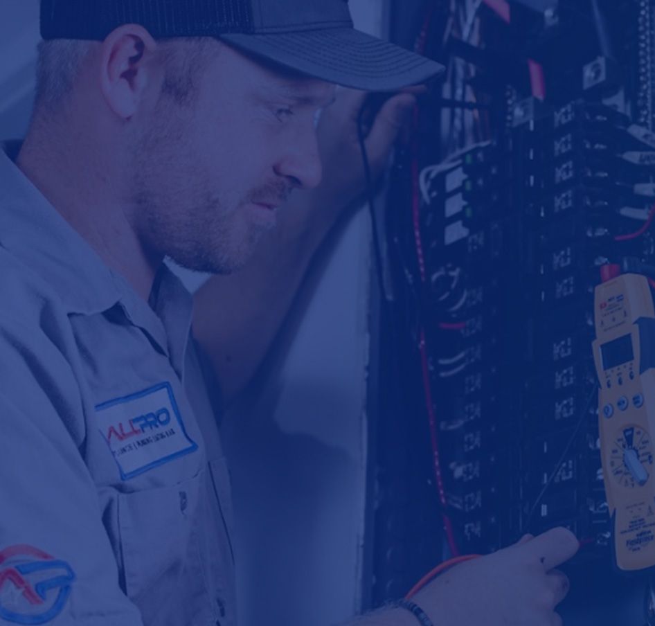 Electrician in blue work shirt, inspecting an electrical panel, focused expression.