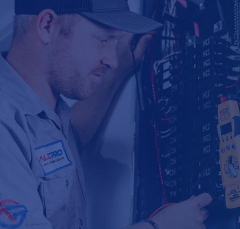 Electrician in blue work shirt, inspecting an electrical panel, focused expression.