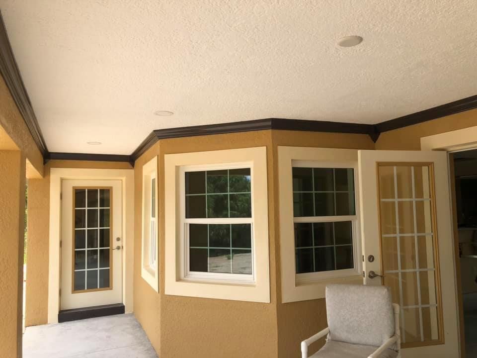 A tan room with white trim and windows. Dark brown trim lines the ceiling. A white chair sits inside.