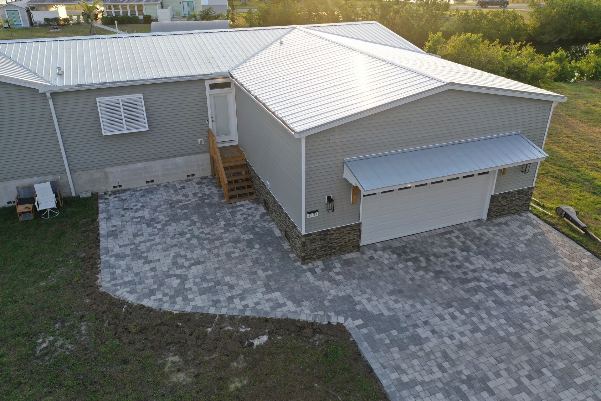 Gray and white house with metal roof and paver driveway.