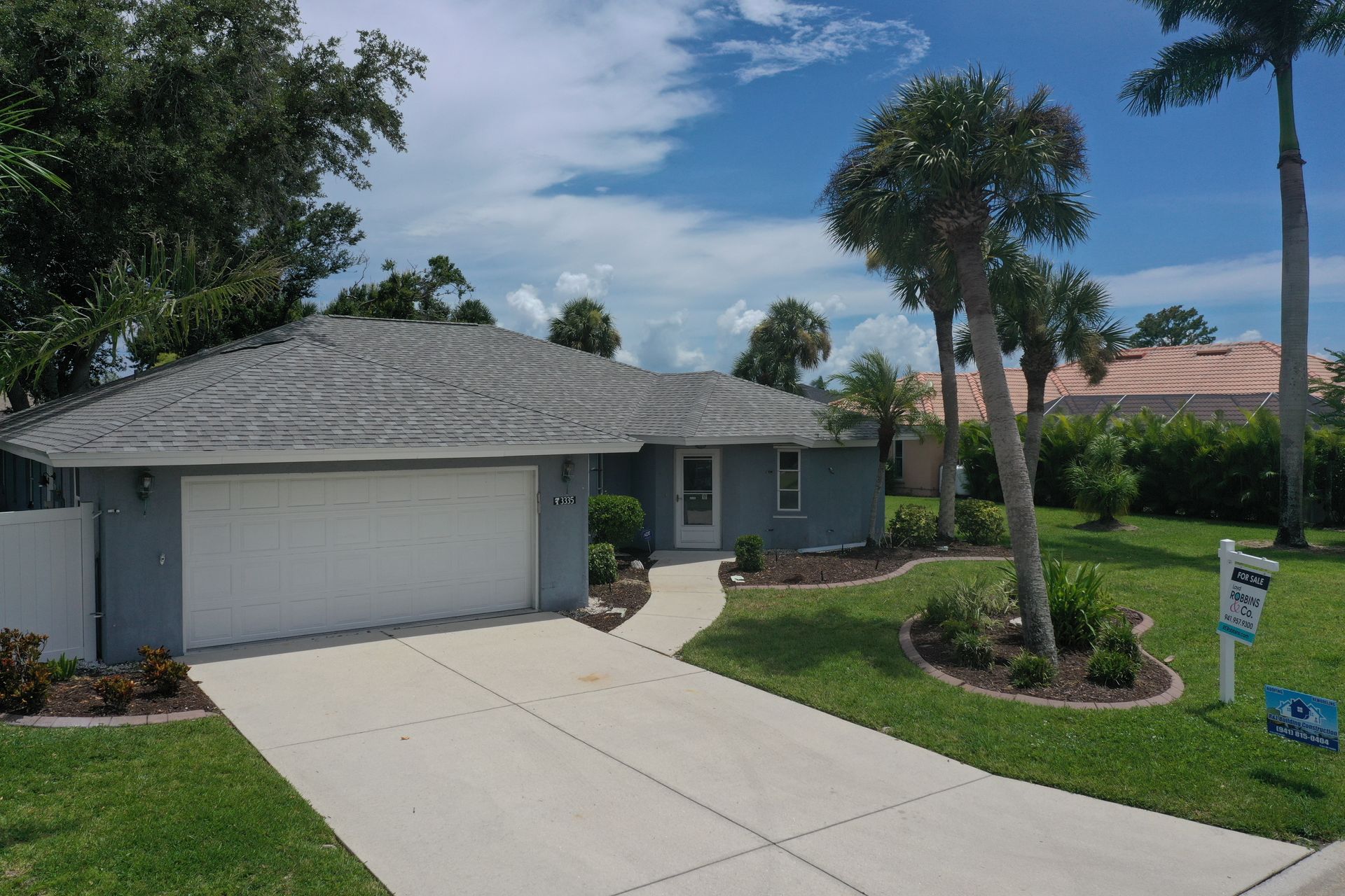 Blue house with white garage door, concrete driveway, and palm trees under a blue sky.