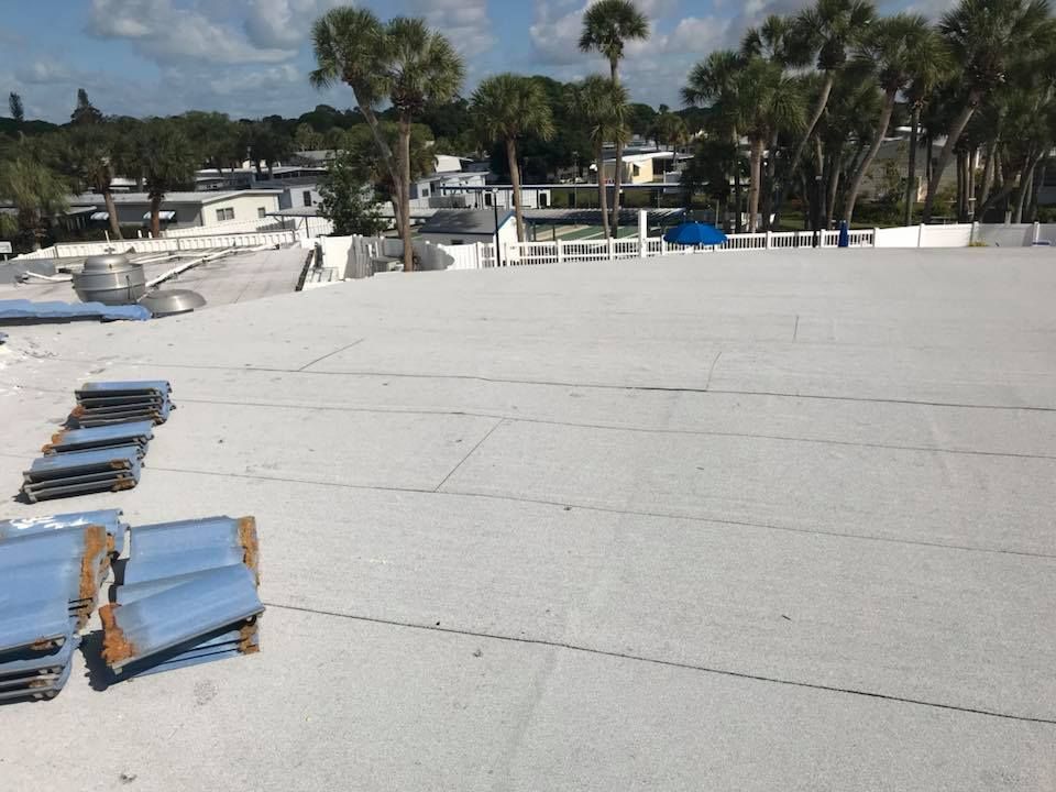 White flat roof with blue tiles, trees, and buildings in the background under a partly cloudy sky.