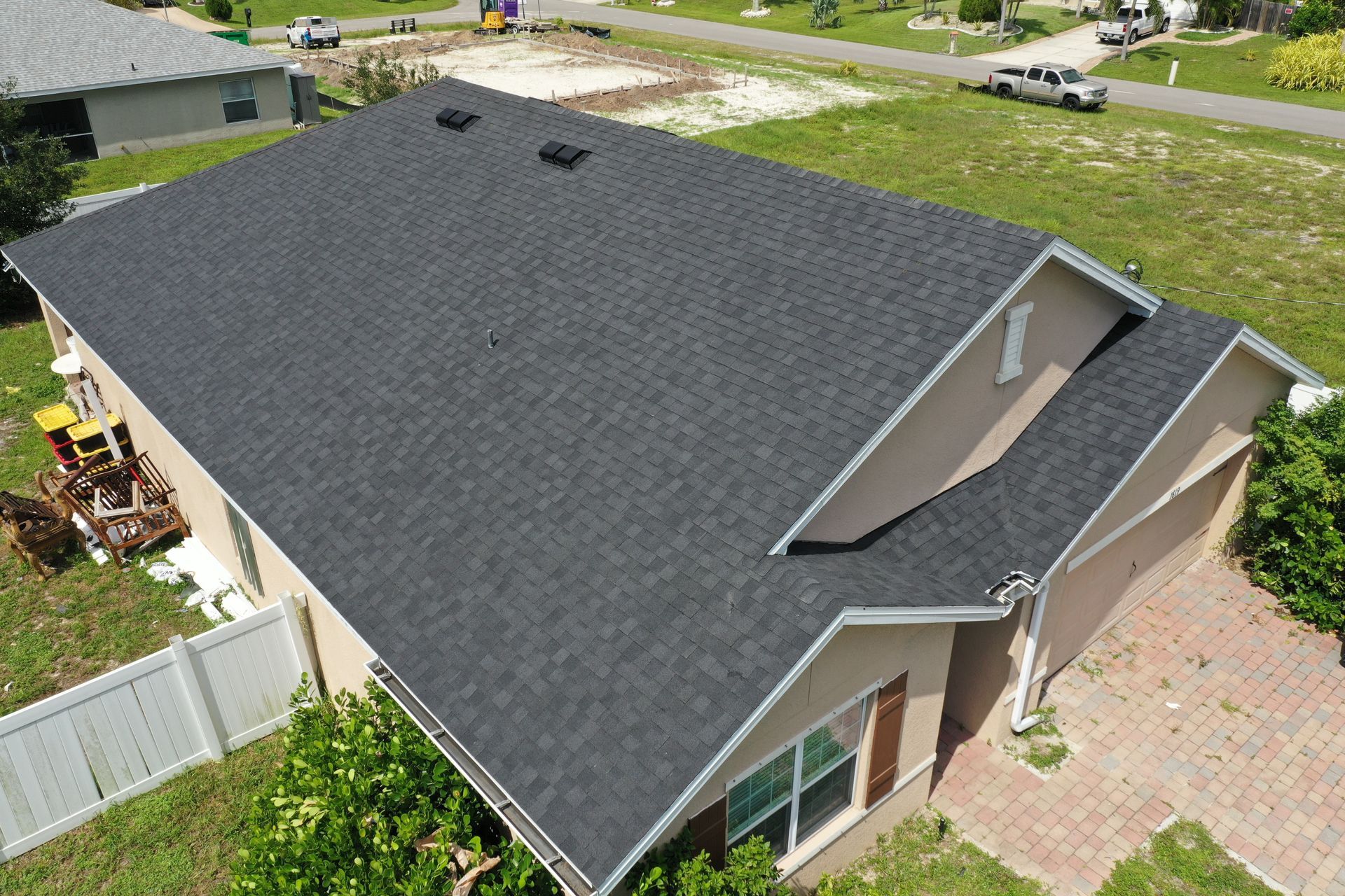Dark gray shingled roof on a tan house with white trim and a small yard.