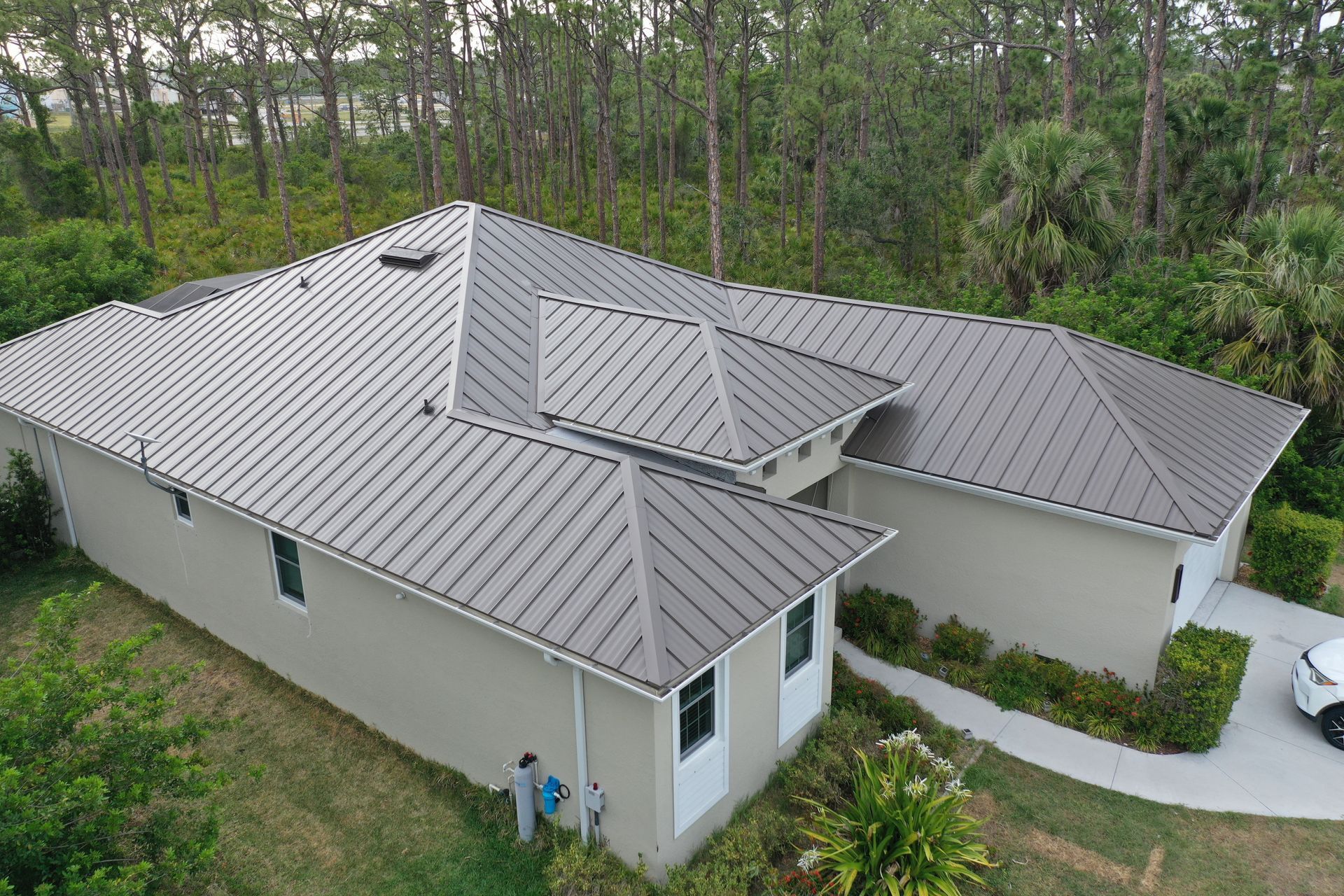 Beige house with gray metal roof; driveway leads to white car.