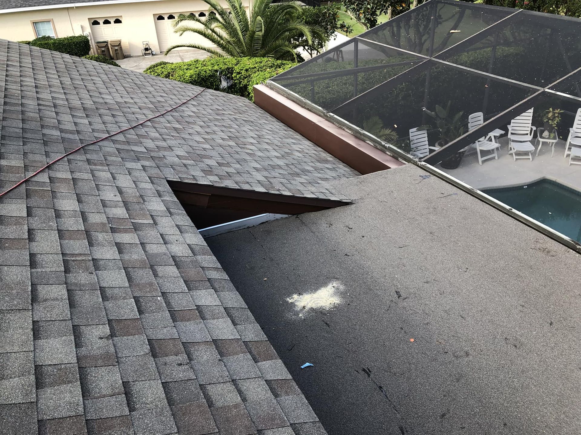Overhead view of a shingled roof with a large hole and a swimming pool enclosure in the background.