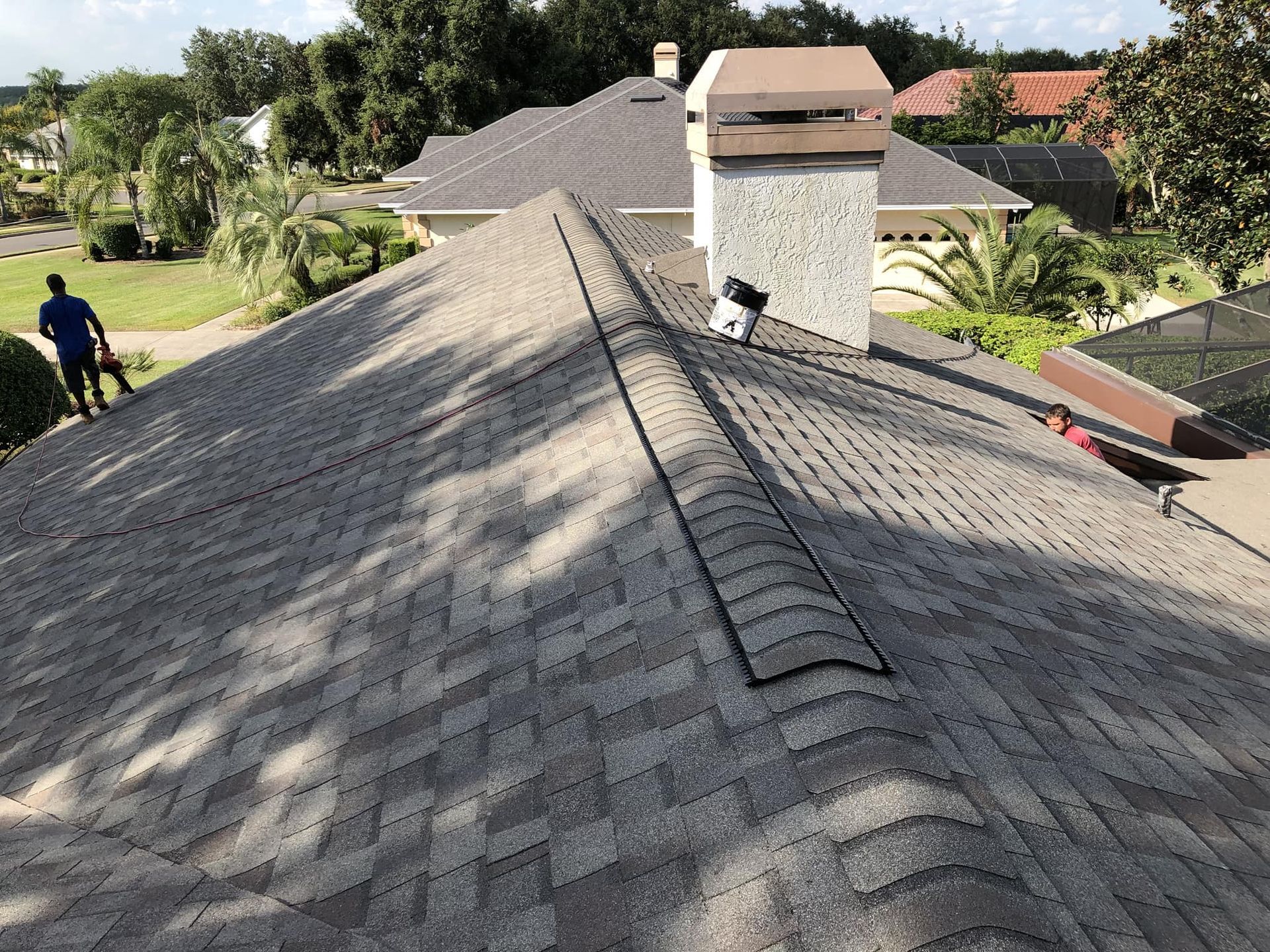 Roof with shingles, chimney, and person blowing debris with yard in background.