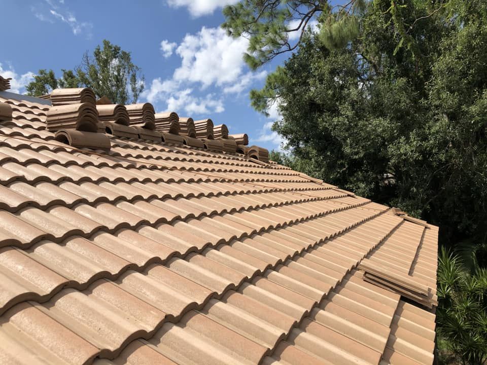 Tan tile roof under blue sky with white clouds and green trees.
