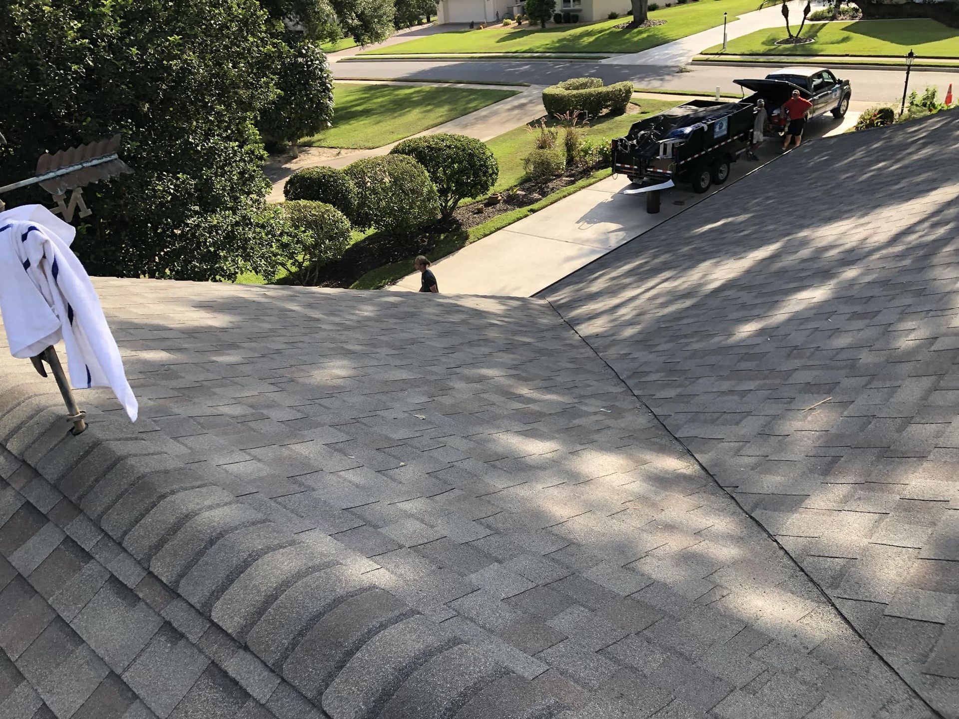 Rooftop with grey shingles. Vehicles parked in driveway. Trees and residential street in the background.