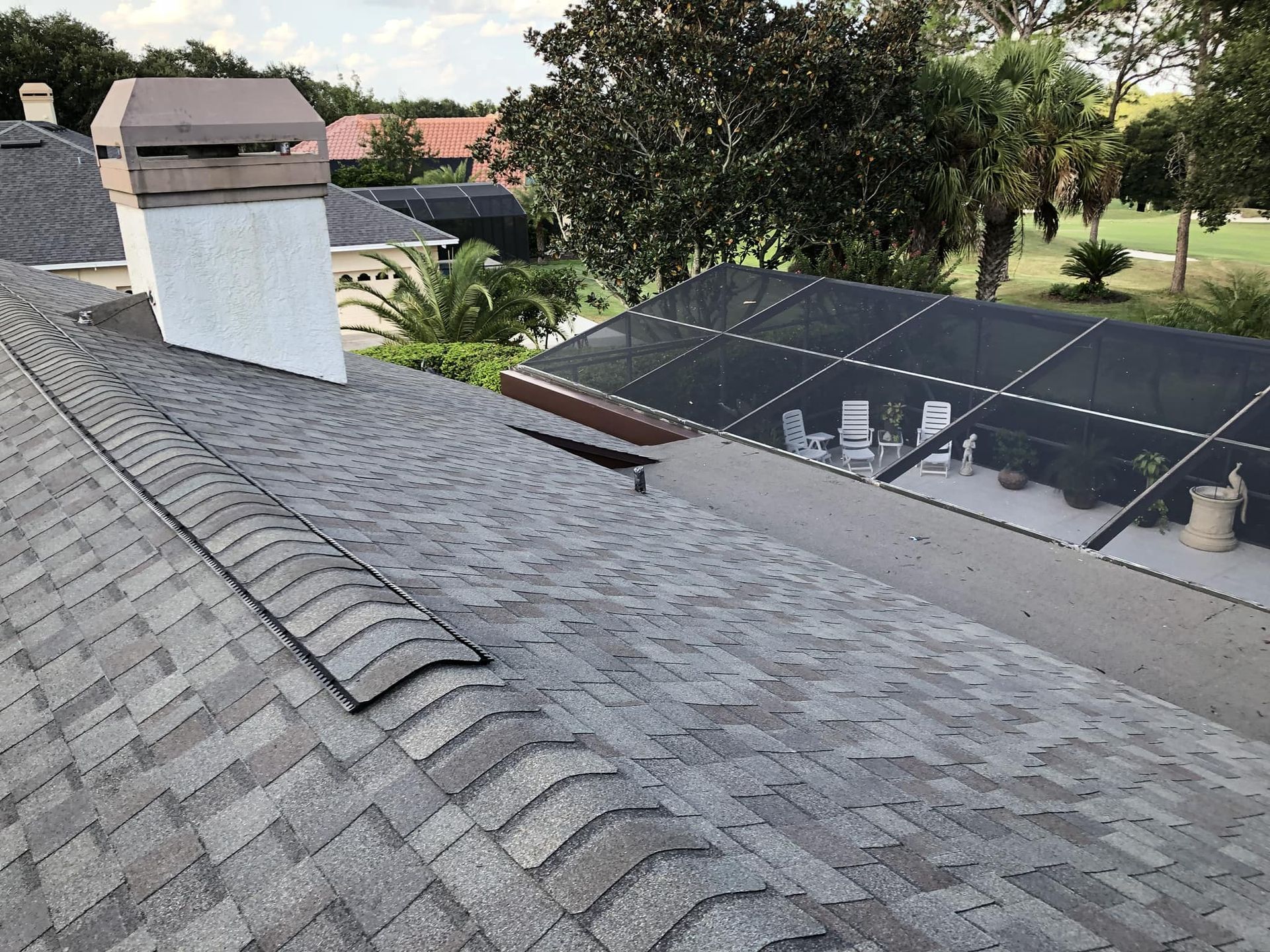 Gray asphalt shingle roof with chimney and view of a pool enclosure and neighborhood.