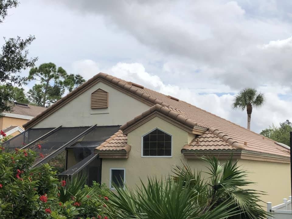 Tan house with a tile roof, a screened-in porch, and palm trees against a cloudy sky.