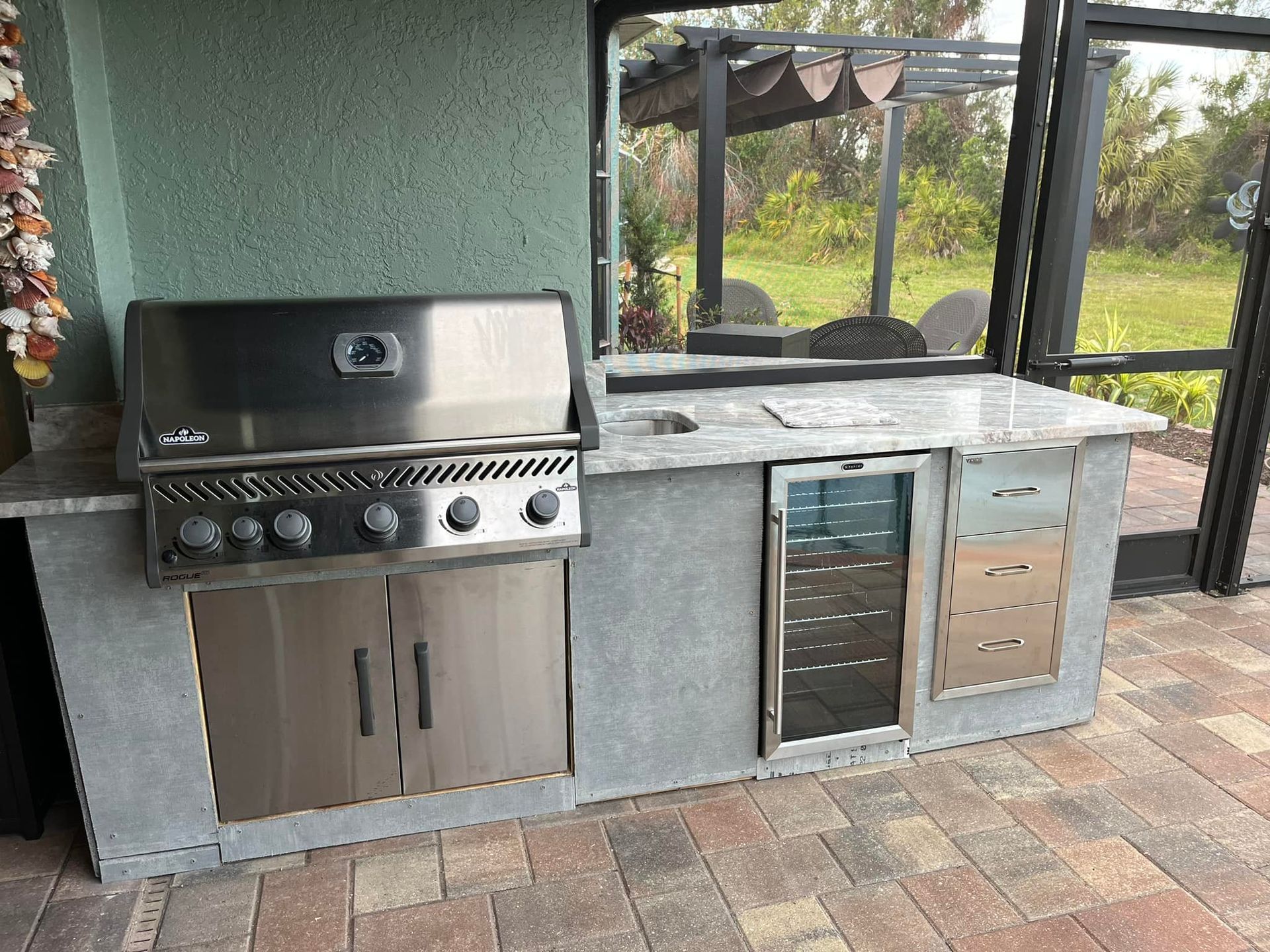 Outdoor kitchen with stainless steel grill, refrigerator, and countertop.