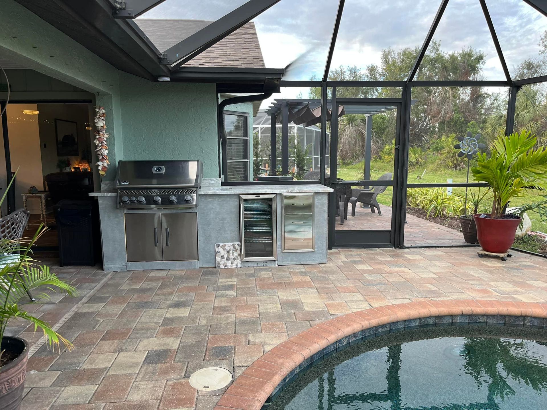 Outdoor kitchen with grill, refrigerator, and pool in a screened patio.