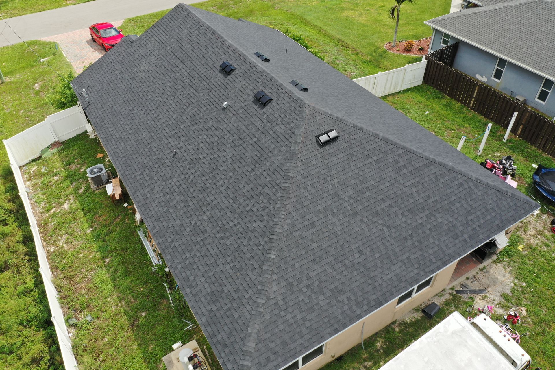 Overhead view of a house with a dark gray shingled roof, surrounded by grass and a white fence.