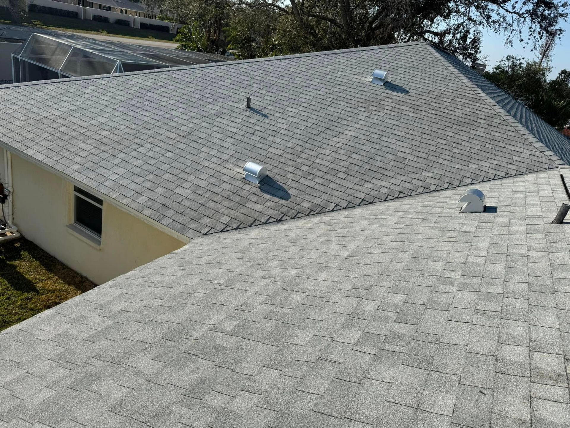 Gray asphalt shingle roof with several vents on a sunny day.