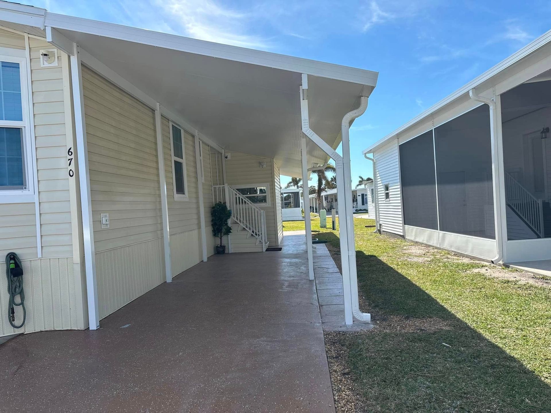 A covered walkway between two light-colored buildings, with a concrete floor and green lawn to the right.