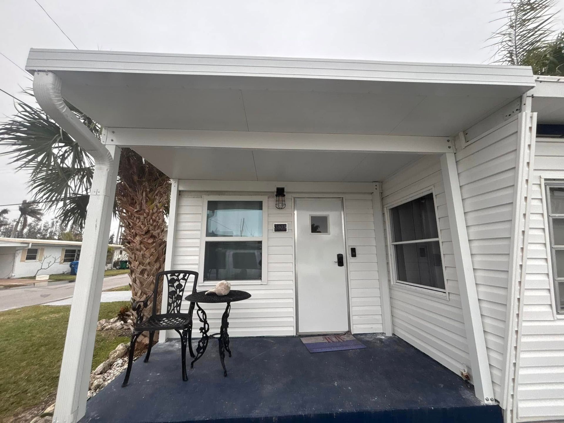 White building with porch, black table and chair. Door is centered, with windows on either side.
