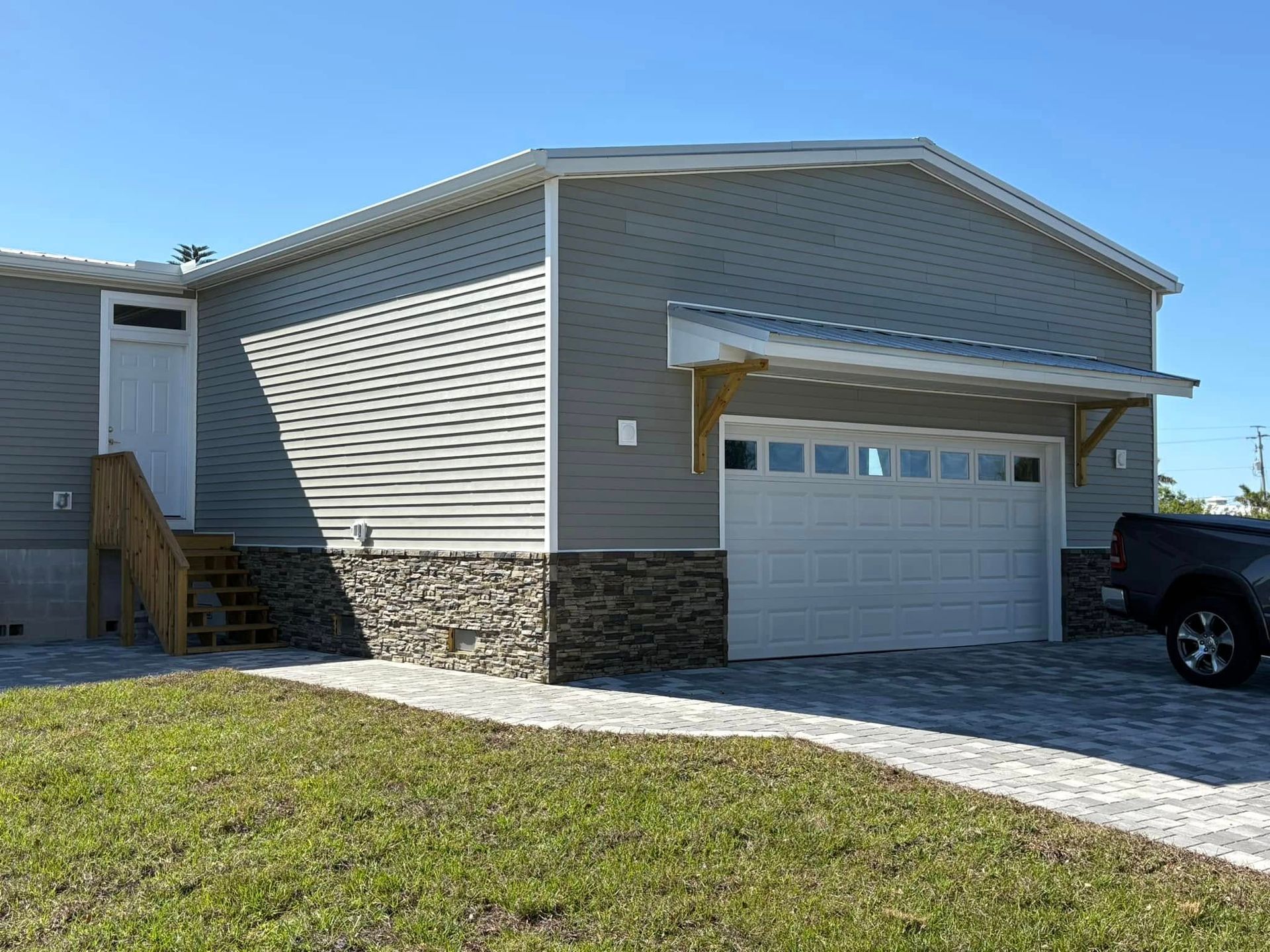 Gray house with stone base and garage door; driveway and lawn in front.