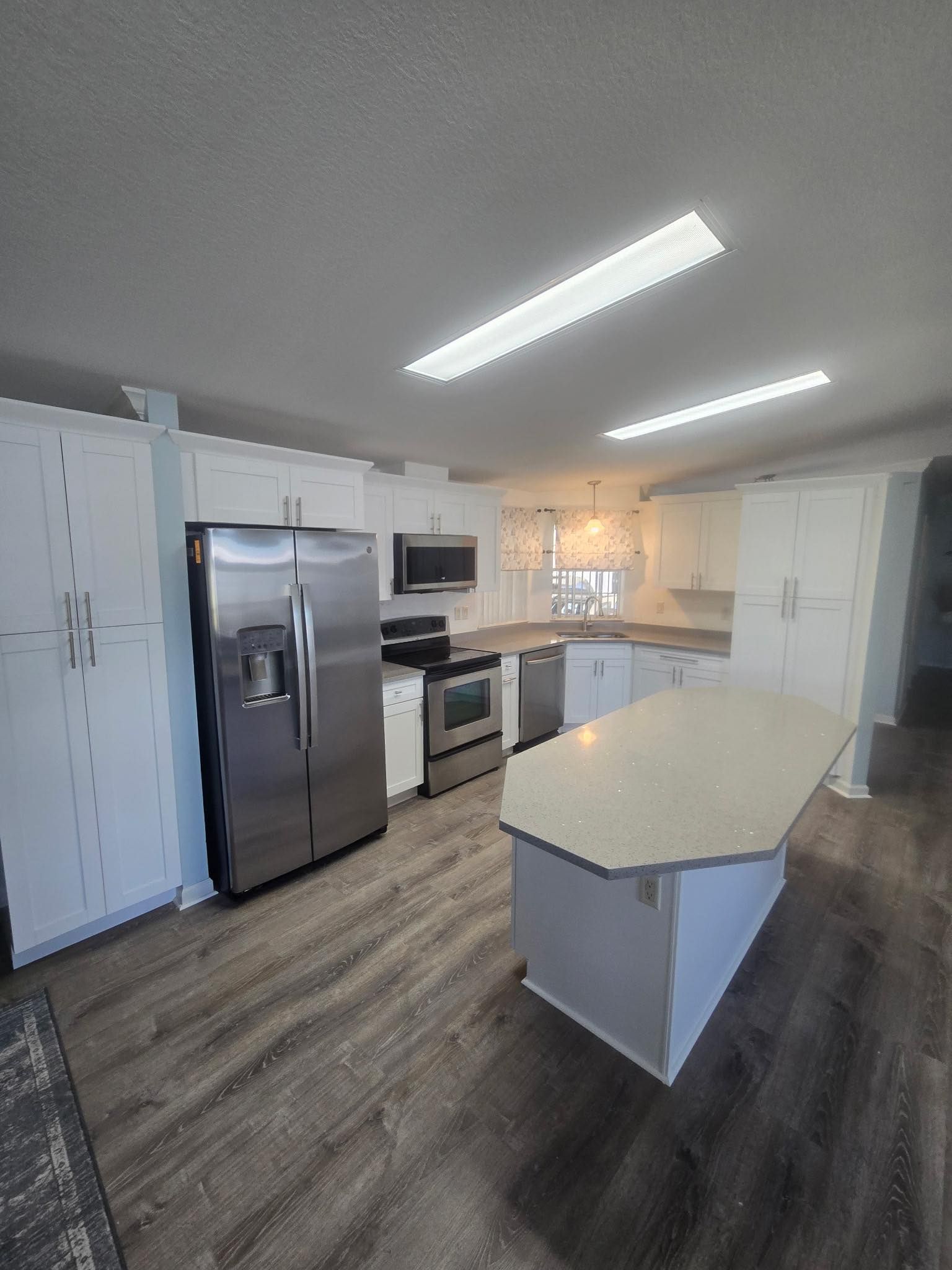 White kitchen with stainless steel appliances, gray island and flooring, and white cabinets.
