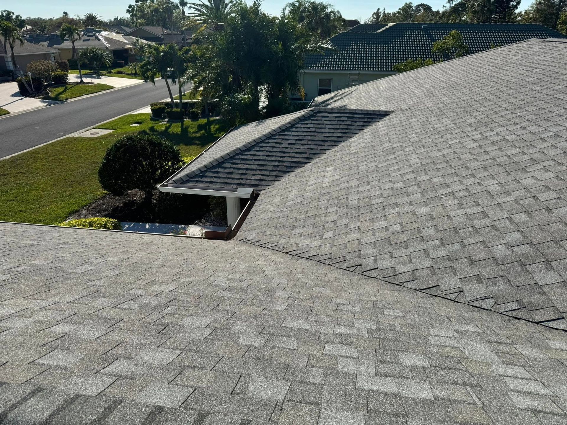 Gray asphalt shingle roof with a skylight, overlooking a residential street with greenery.