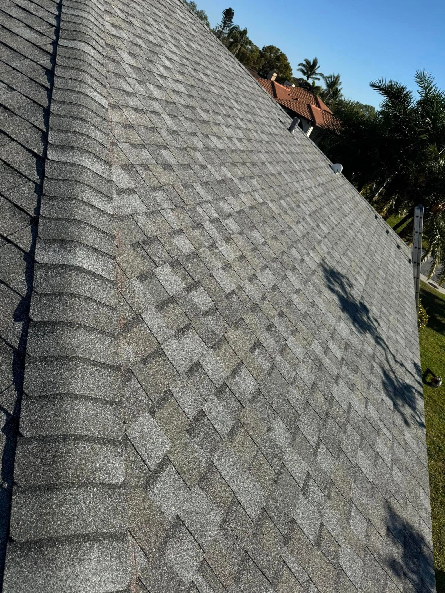 Gray asphalt shingle roof on a house with trees in the background on a sunny day.