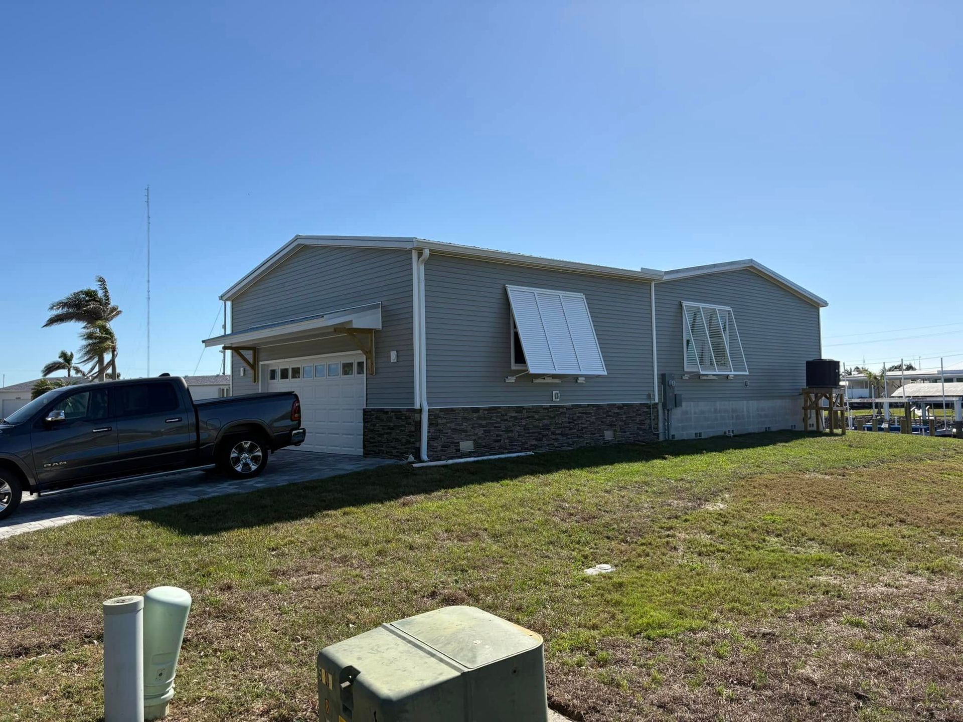 A gray house with boarded windows and a truck parked outside, on a grassy lot.
