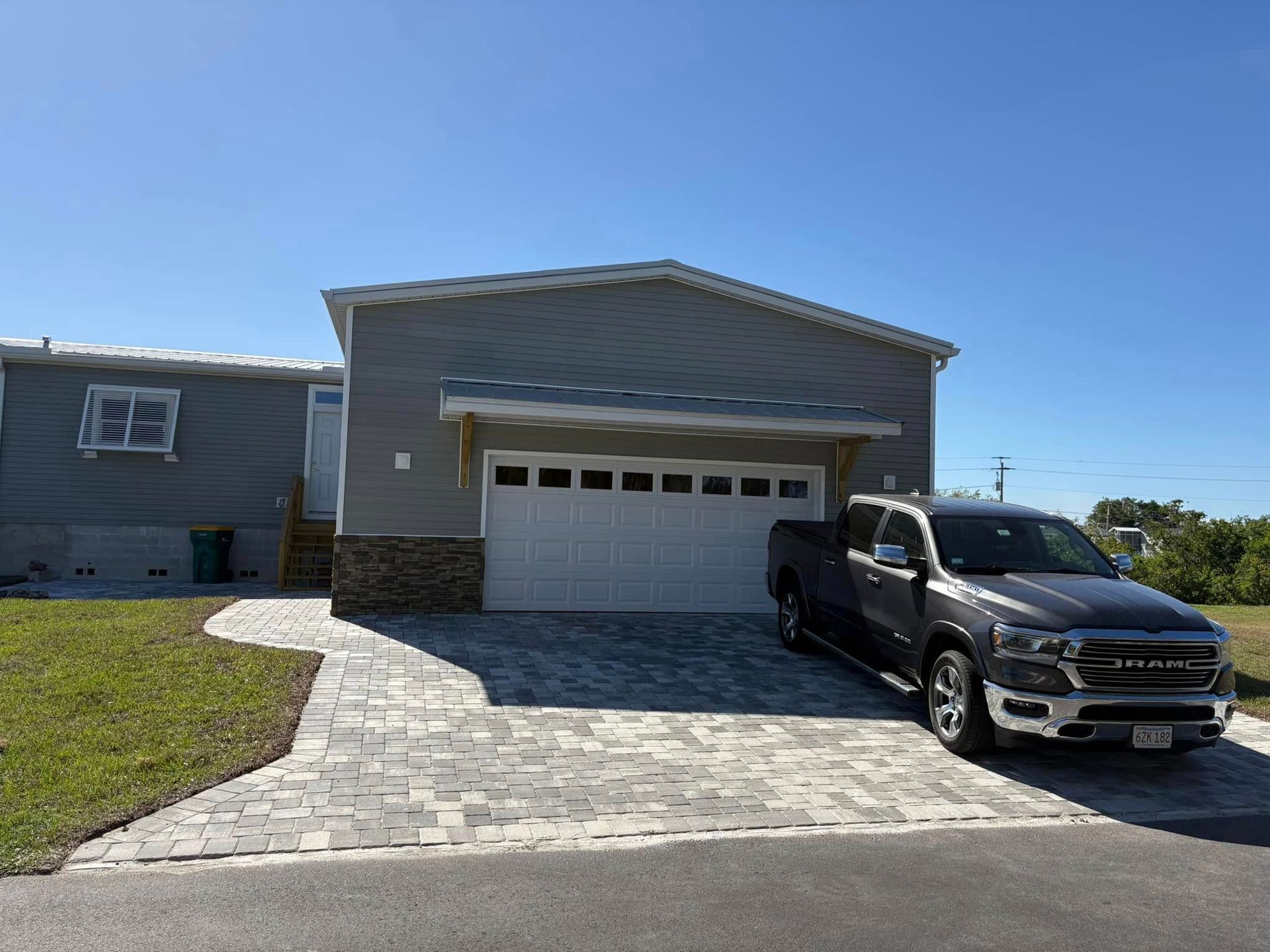 Gray house with driveway, truck, and garage door under a blue sky.