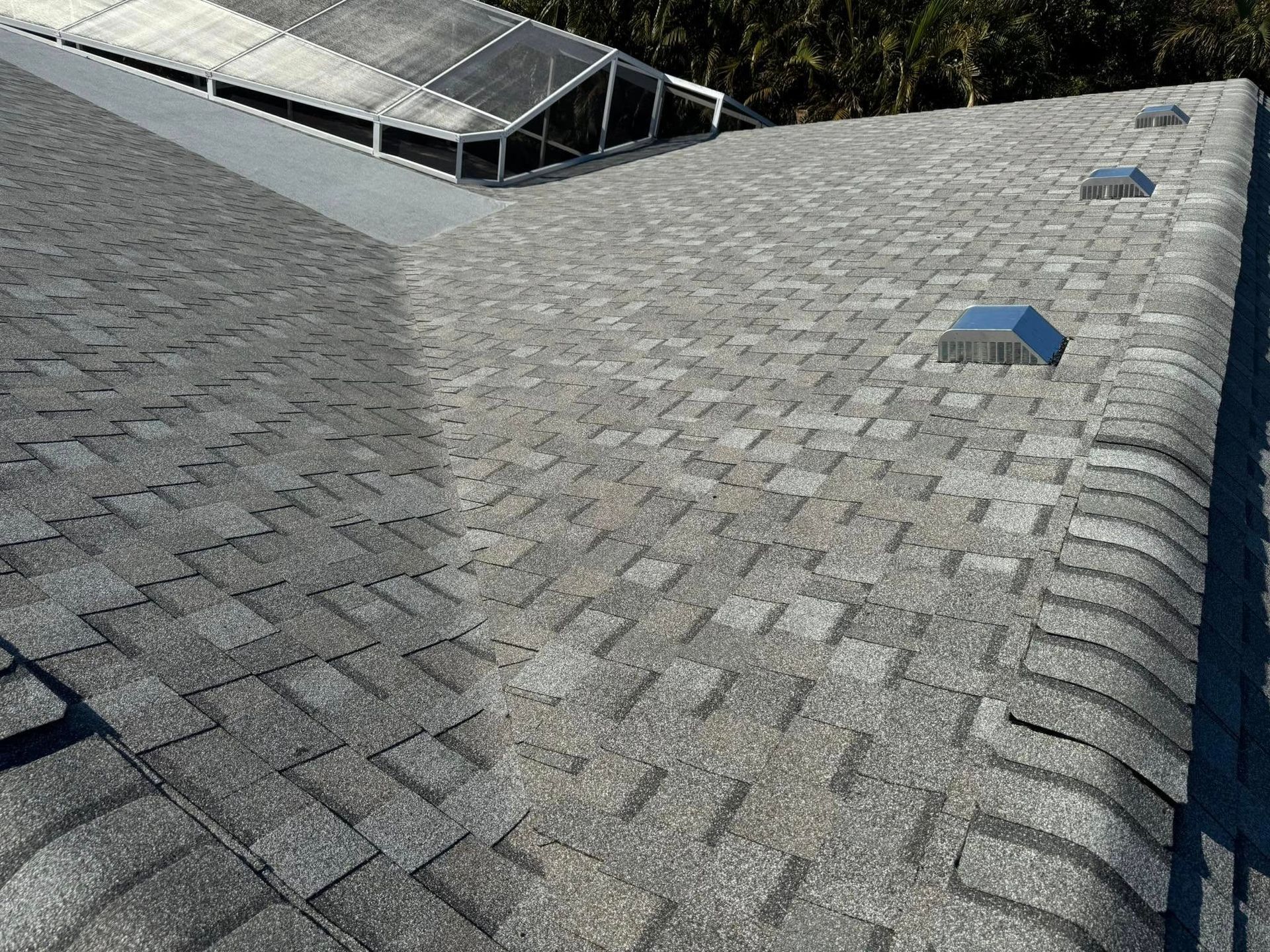 Gray asphalt shingle roof with skylight and vents; bright sunlight.