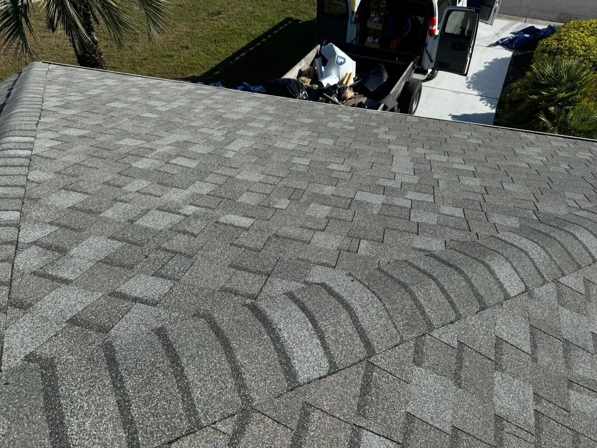 Gray asphalt shingle roof with dark patches; a van with open doors parked nearby.