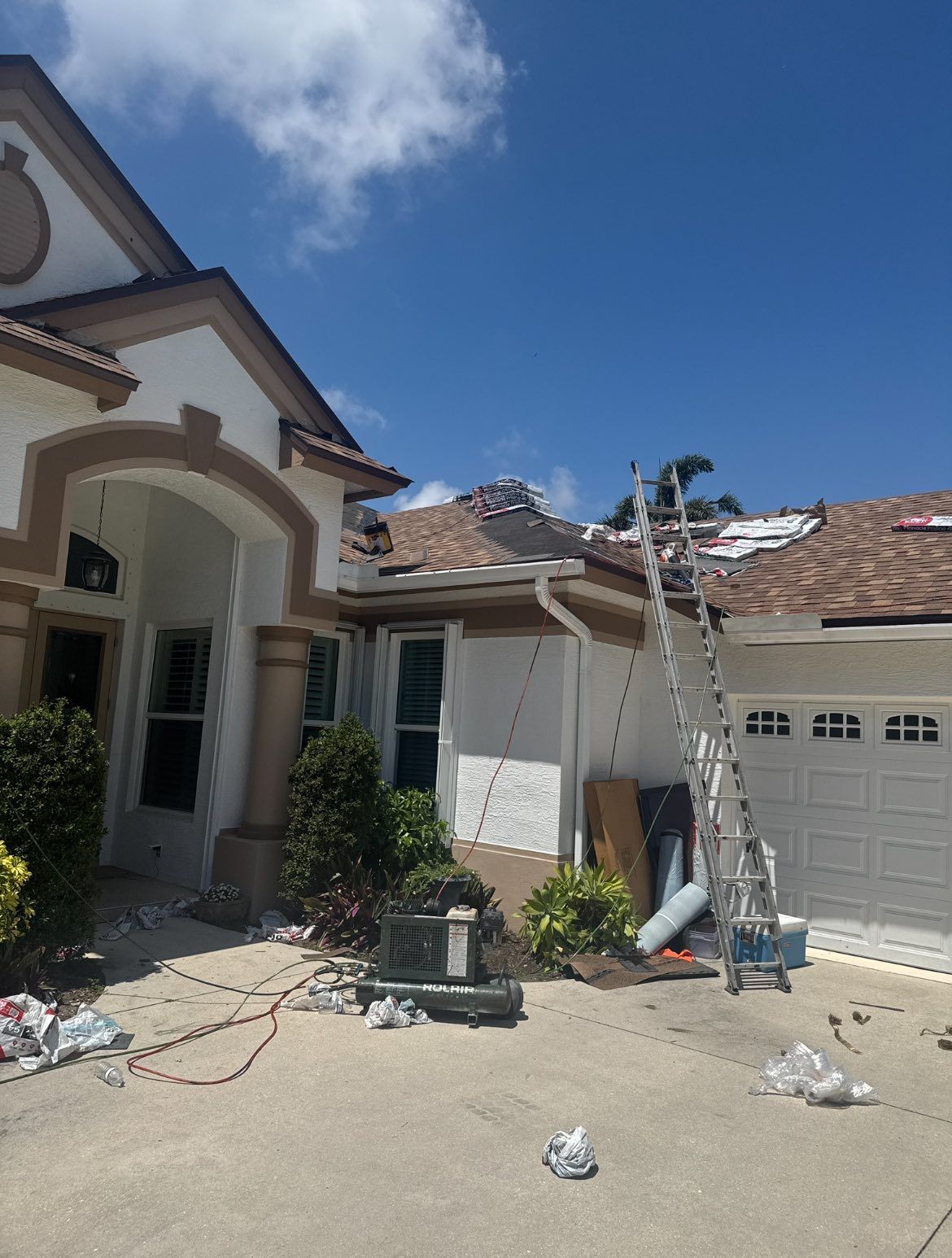 Home with roofing work in progress; brown roof, ladder, clear blue sky.