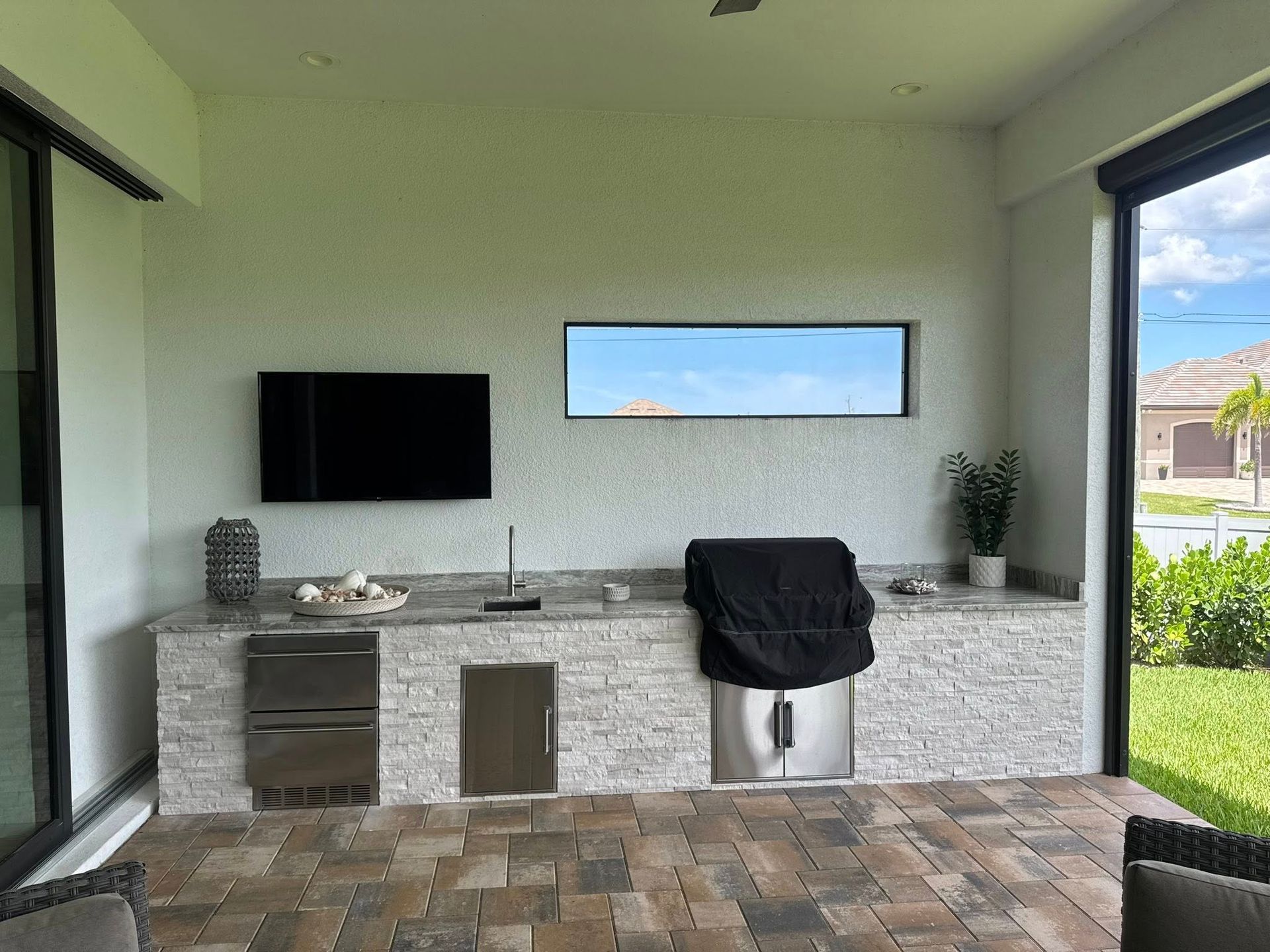 Outdoor kitchen with a grill, sink, TV, and built-in appliances.