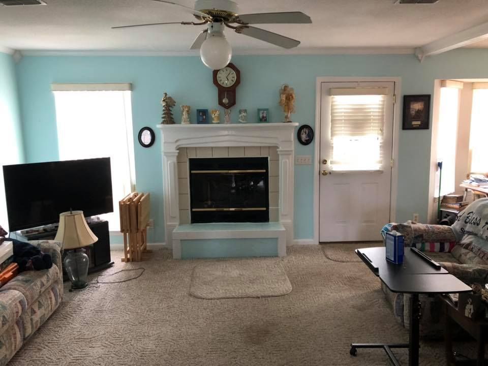 Living room with fireplace, TV, and door. Turquoise walls, tan carpet, and a ceiling fan.