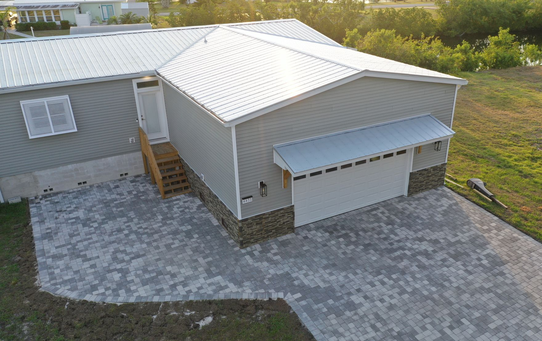 Gray house with metal roof, driveway, and garage door. Exterior with stone accents.