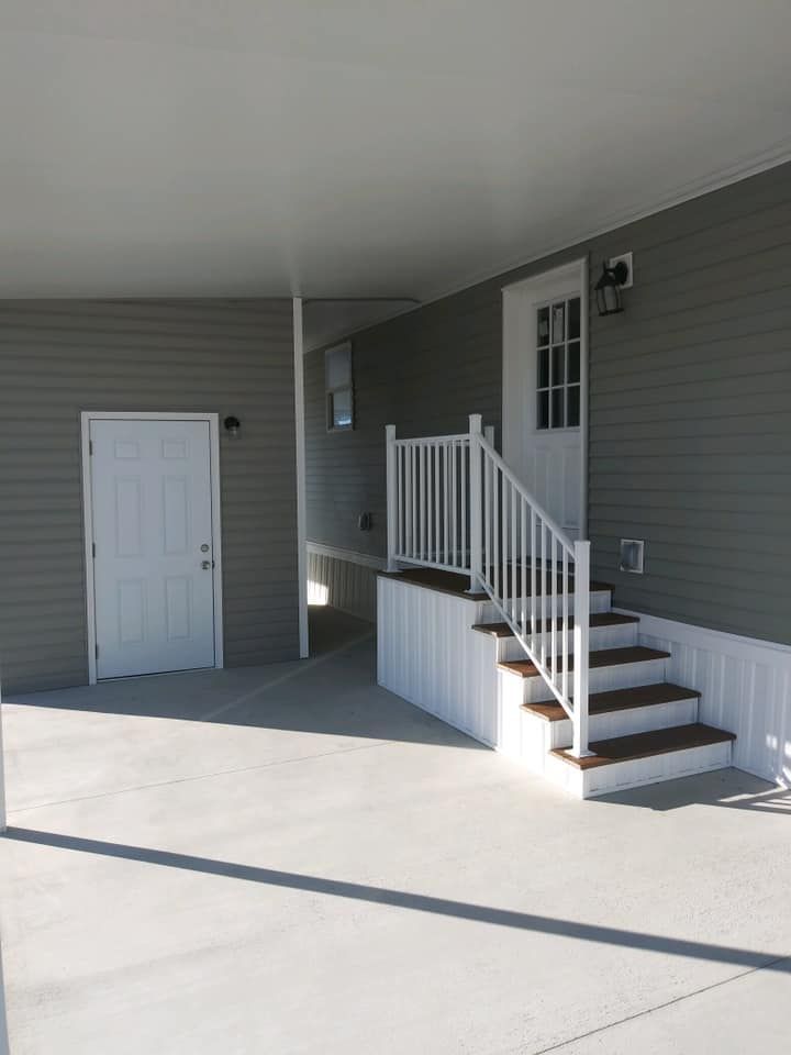 Gray siding with white doors and stairs leading to a door under a carport roof.