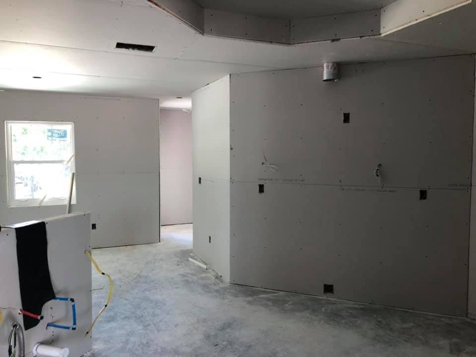 Interior room under construction; drywall installed, electrical boxes visible, unfinished ceiling, concrete floor.