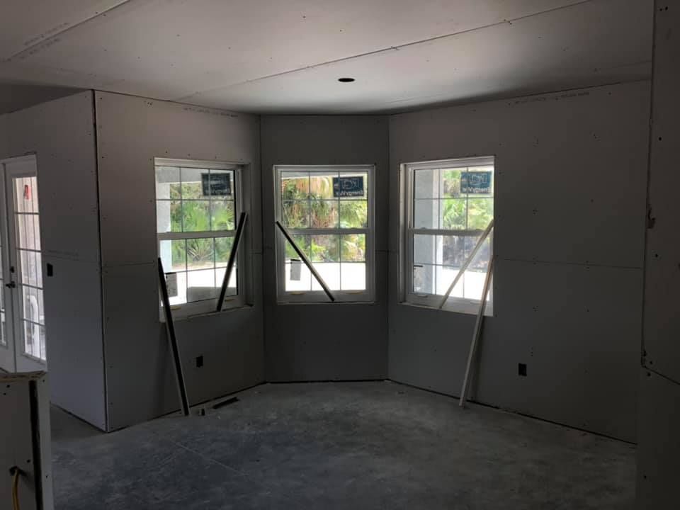 Interior under construction; drywall walls with three windows in a bay; two construction tools propped near the windows.
