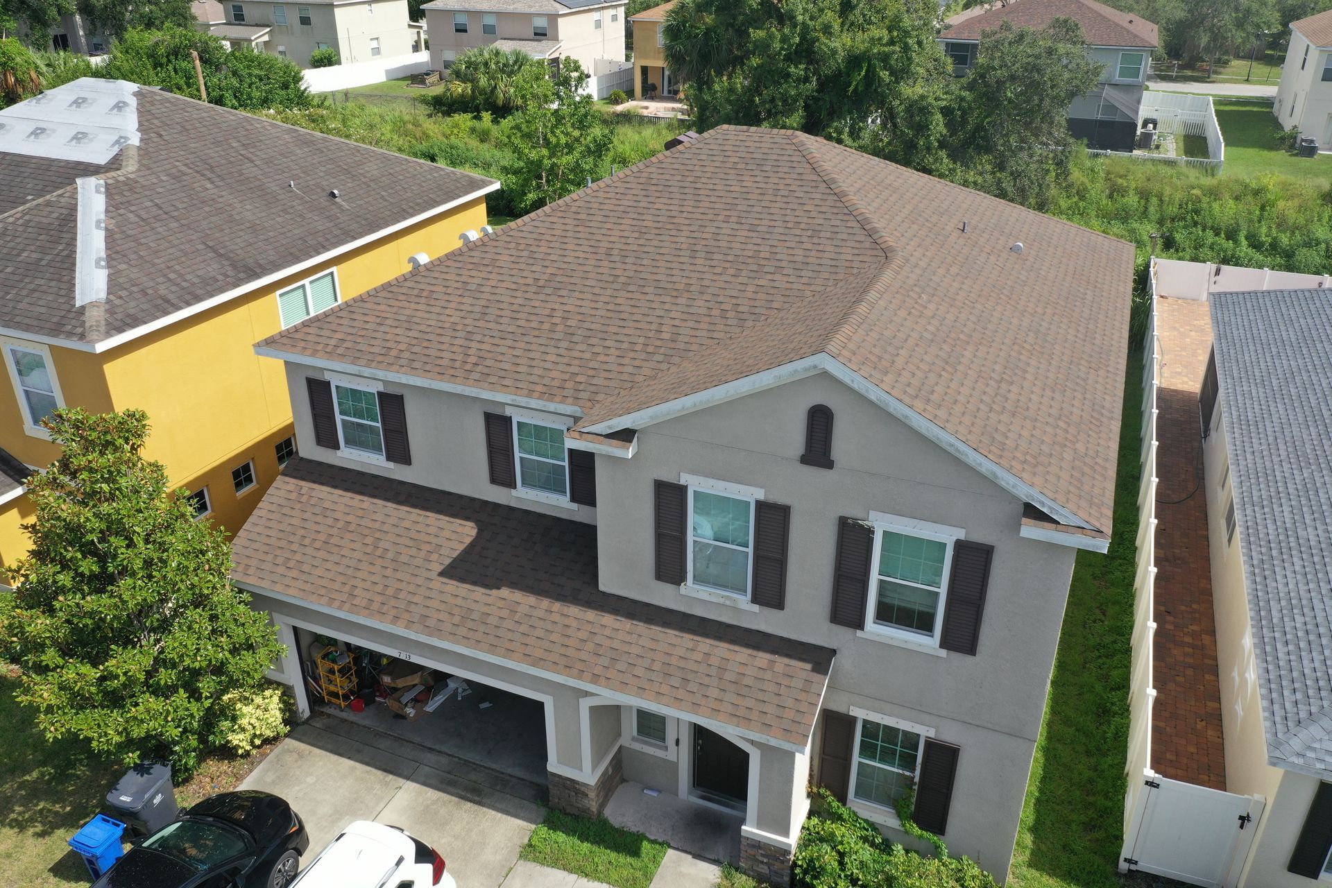 Two-story house with brown roof, beige siding, and dark shutters.