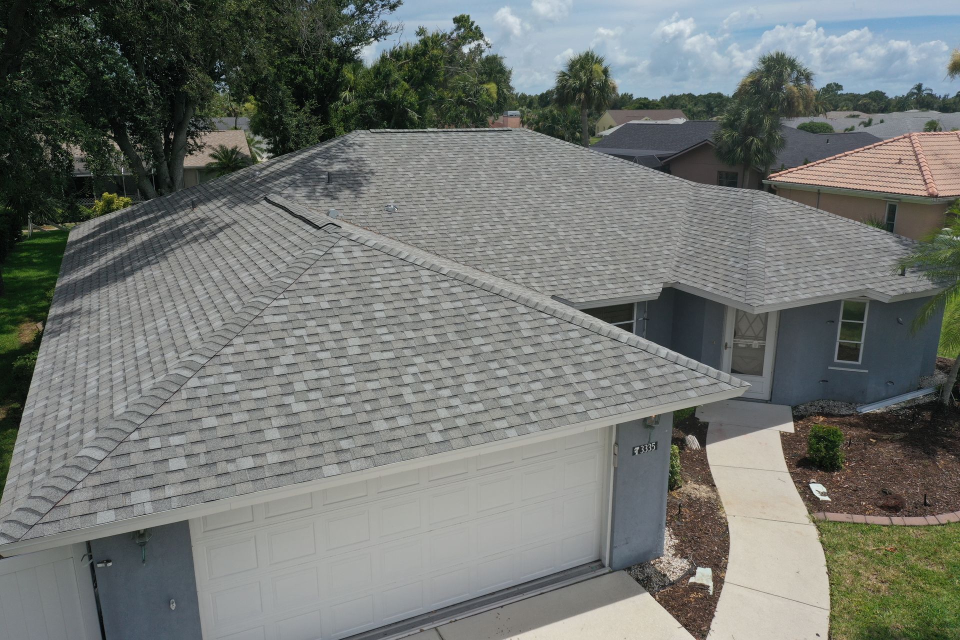 Aerial view of a blue house with a gray roof. A white garage door and walkway are also visible.
