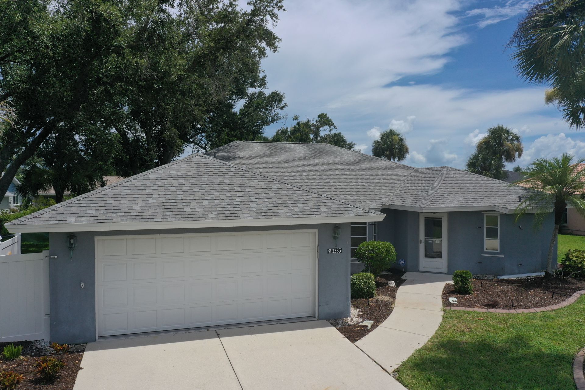 Blue house with gray roof, white garage door, and a curved walkway. Lush green grass and trees.