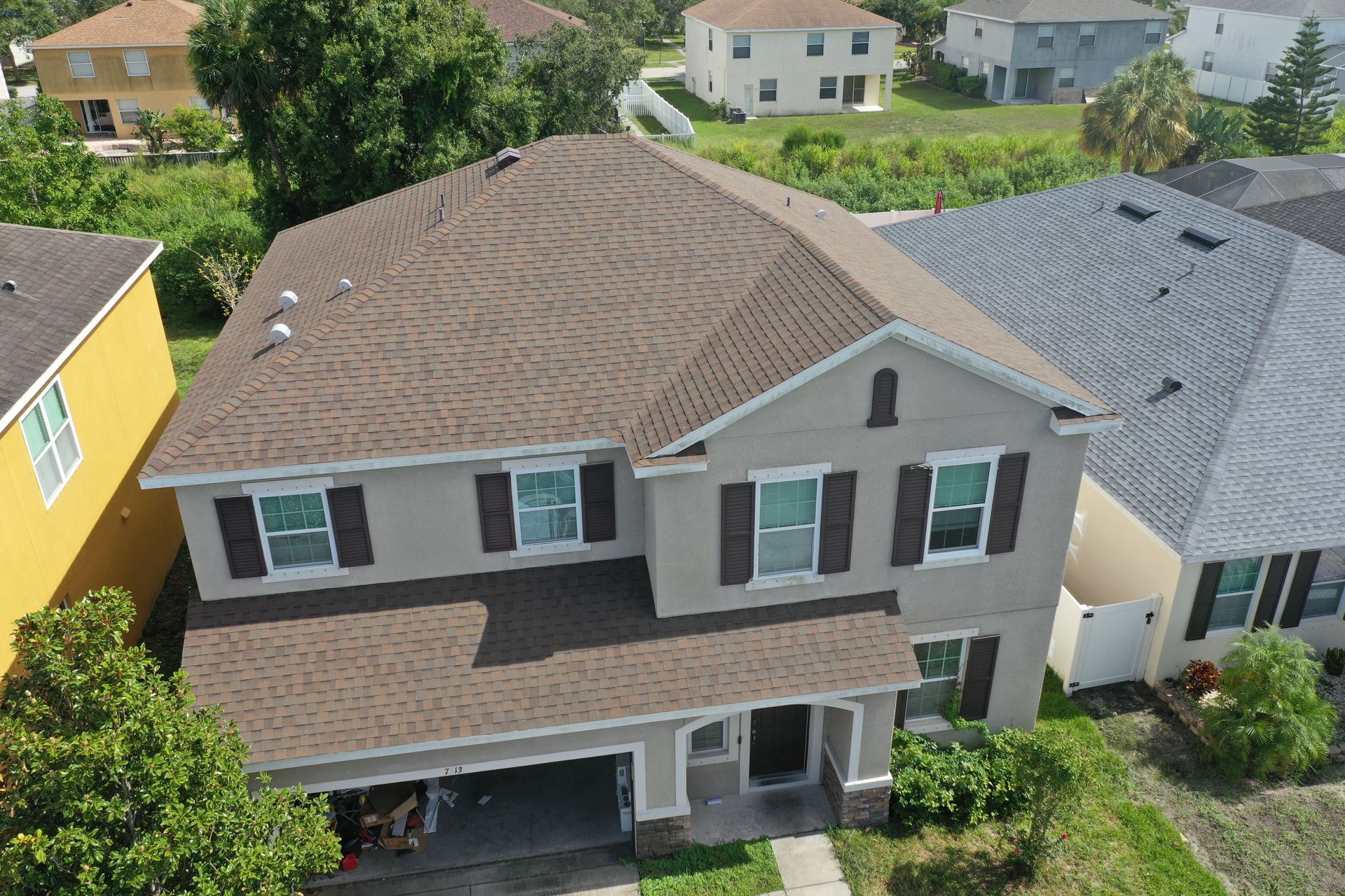 Two-story house with brown roof, tan siding, dark shutters, and a driveway.