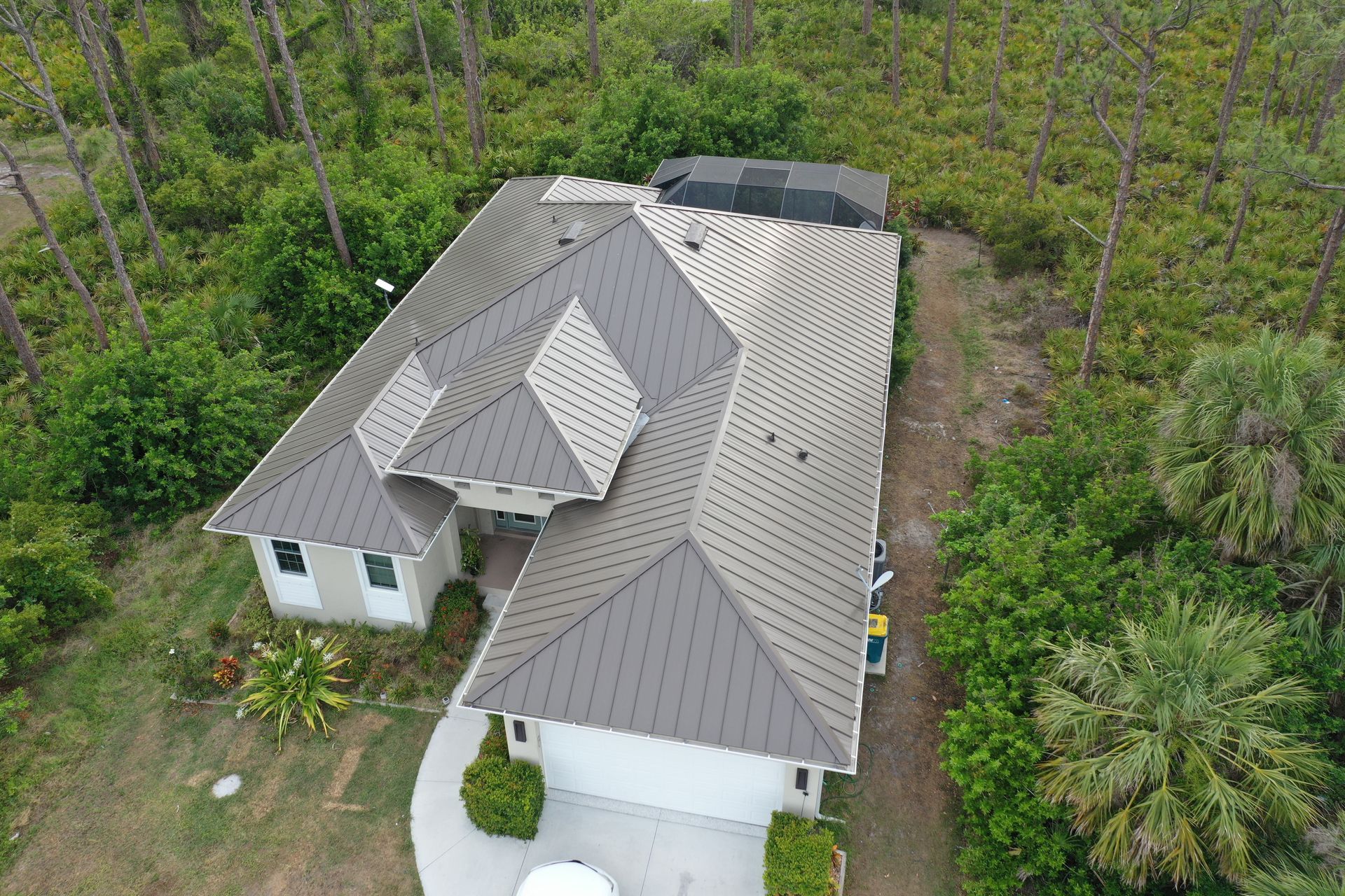 Aerial view of a house with a dark gray metal roof surrounded by trees.