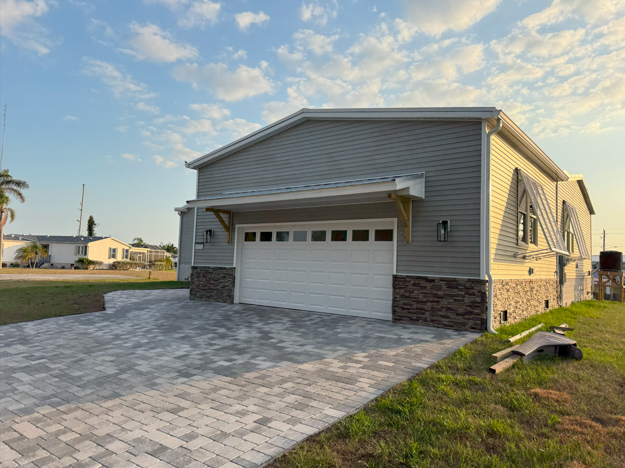 Garage with gray siding, stone veneer, and a brick driveway under a blue sky.