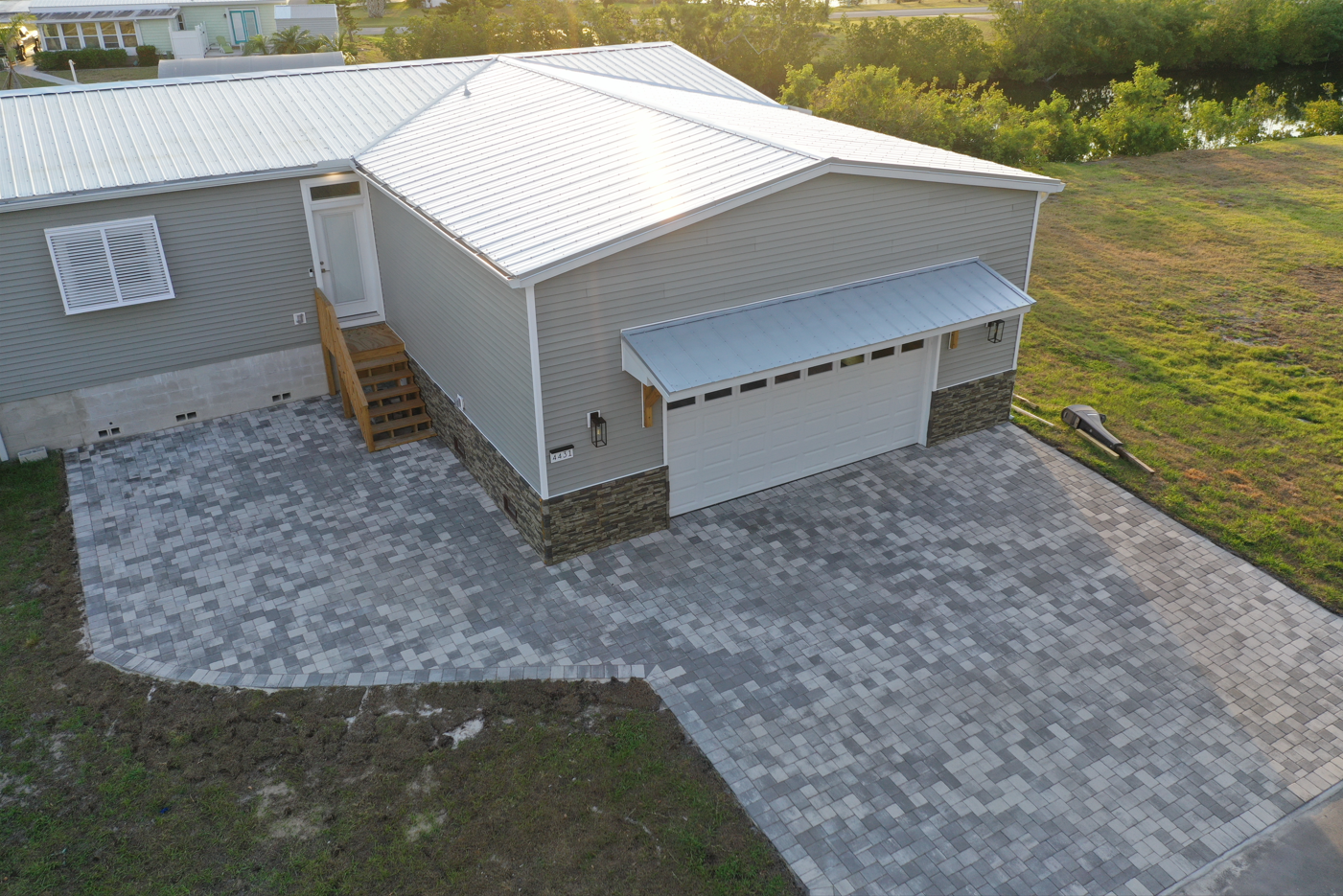 A light gray house with a paved driveway. Metal roof and garage door.