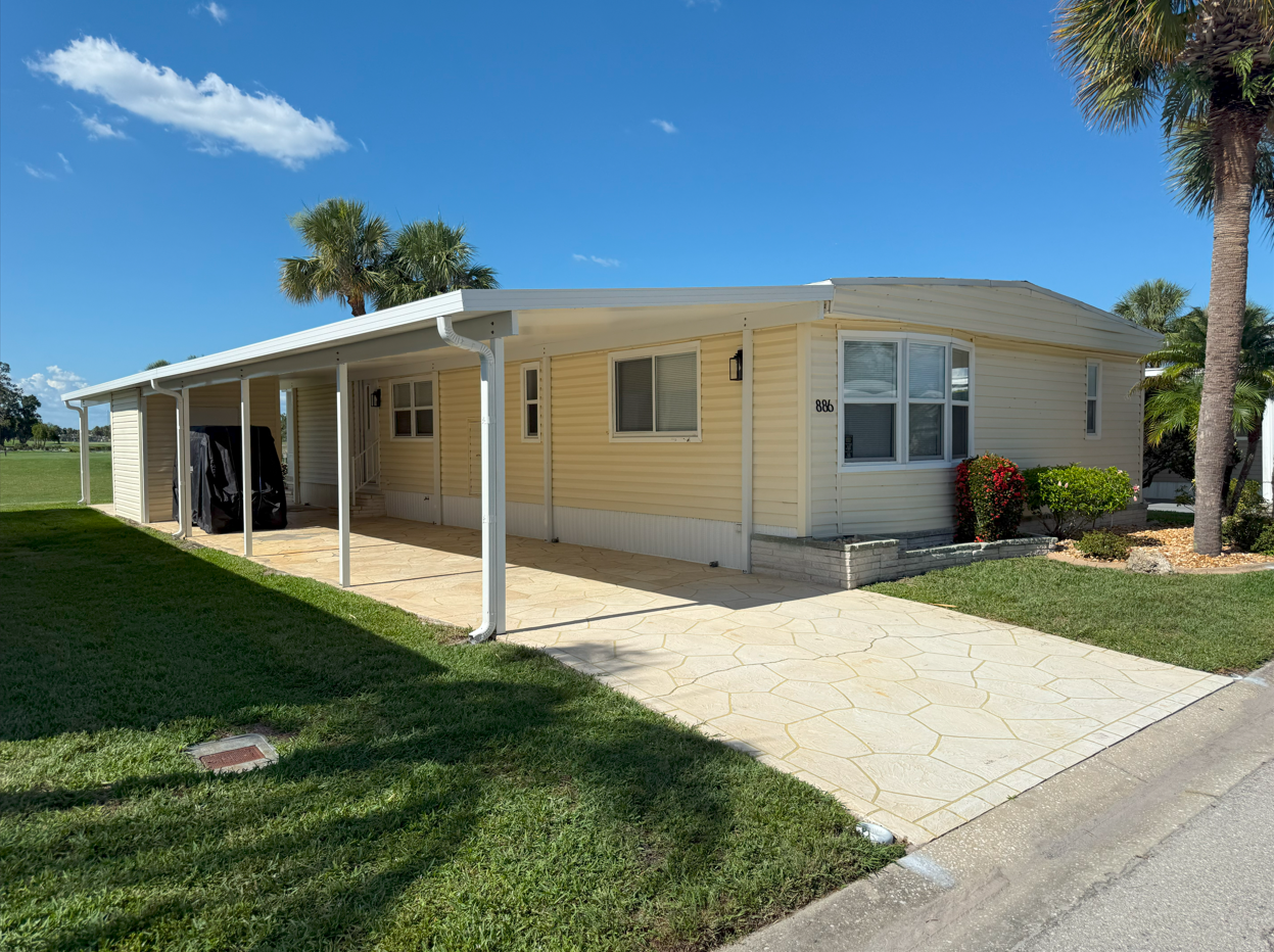 Yellow mobile home with carport and driveway under a blue sky.