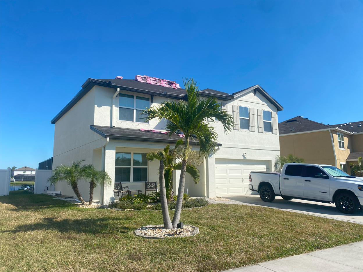 Two-story white house with a partially replaced roof, palm tree in front, white truck parked in the driveway.